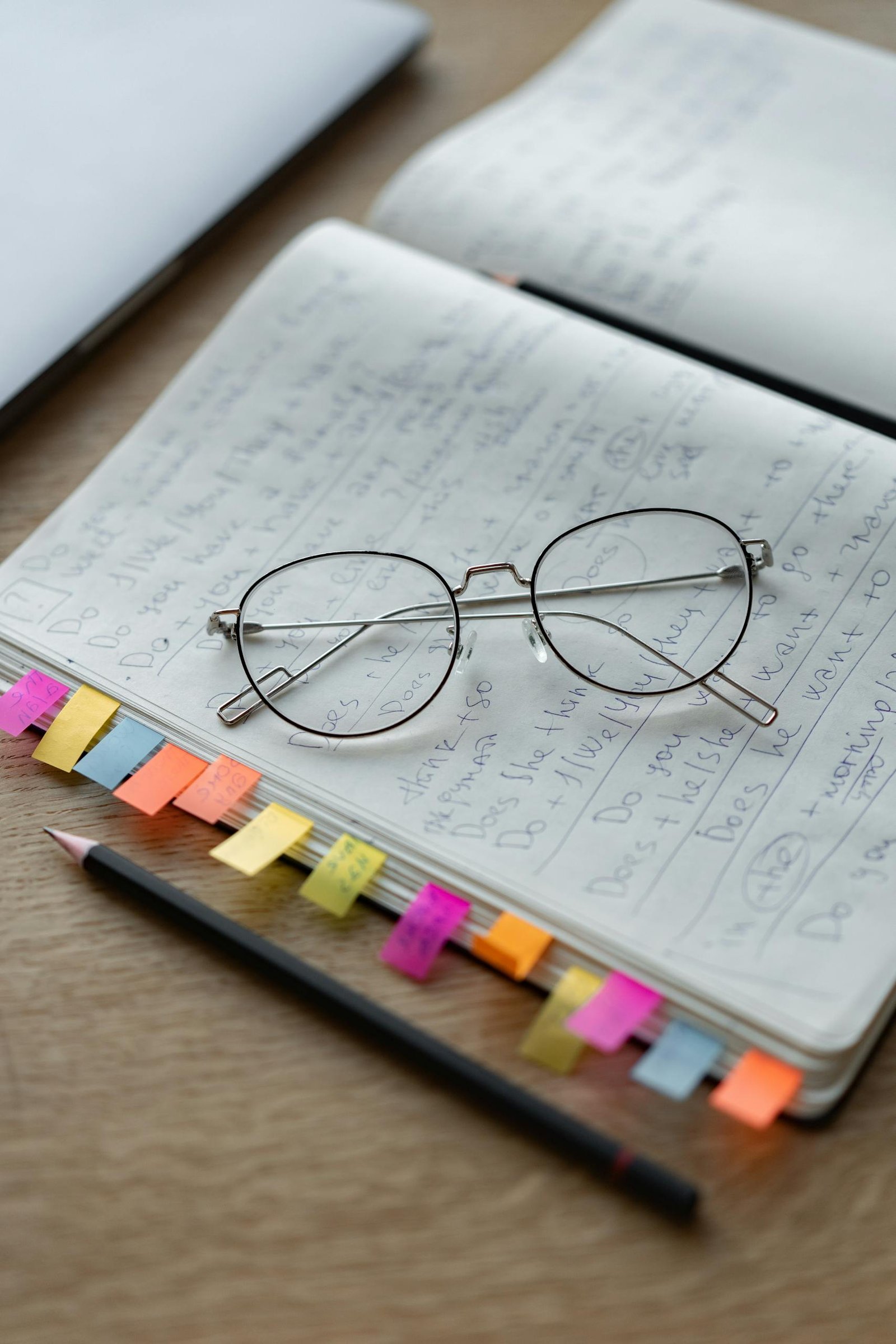 Eyeglasses resting on an open notebook with colorful tabs and pencils creating an educational workspace vibe.