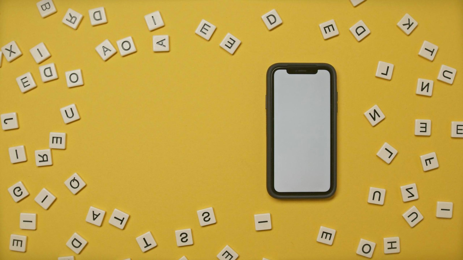 Smartphone surrounded by scattered alphabet tiles on a vibrant yellow background.