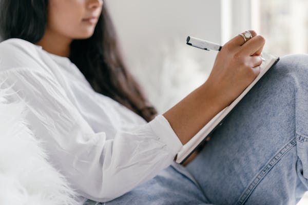 Close-up of a woman writing in a notebook, seated comfortably indoors. Ideal for study and focus themes.